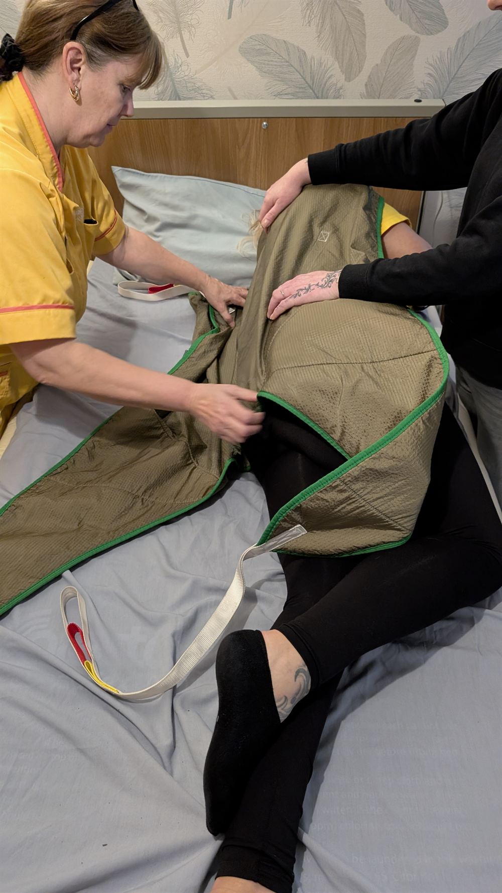 Fitting a sling to a person lying on a bed