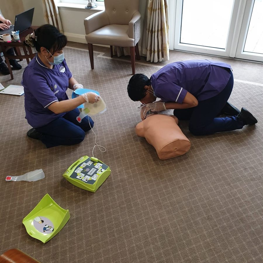 Two nurses practising CPR on a manikin with a training defibrillator during emergency training