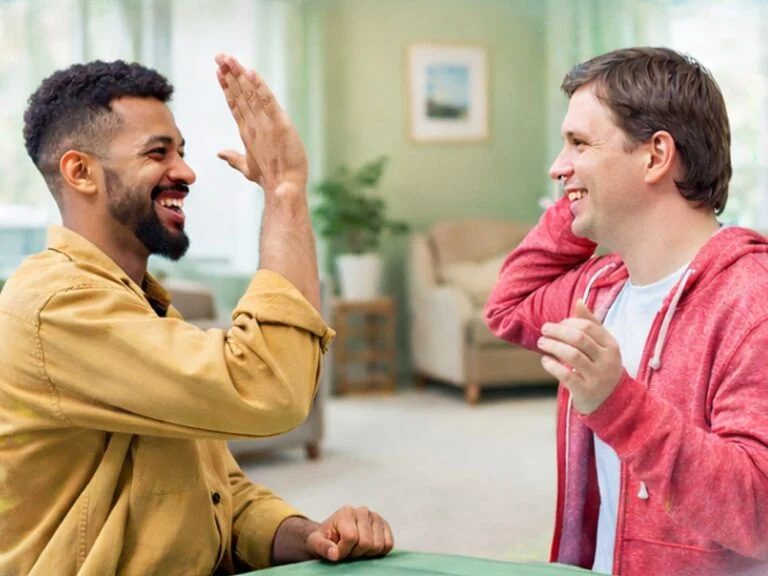 Two smiling men sharing a high five at a table in a bright lounge