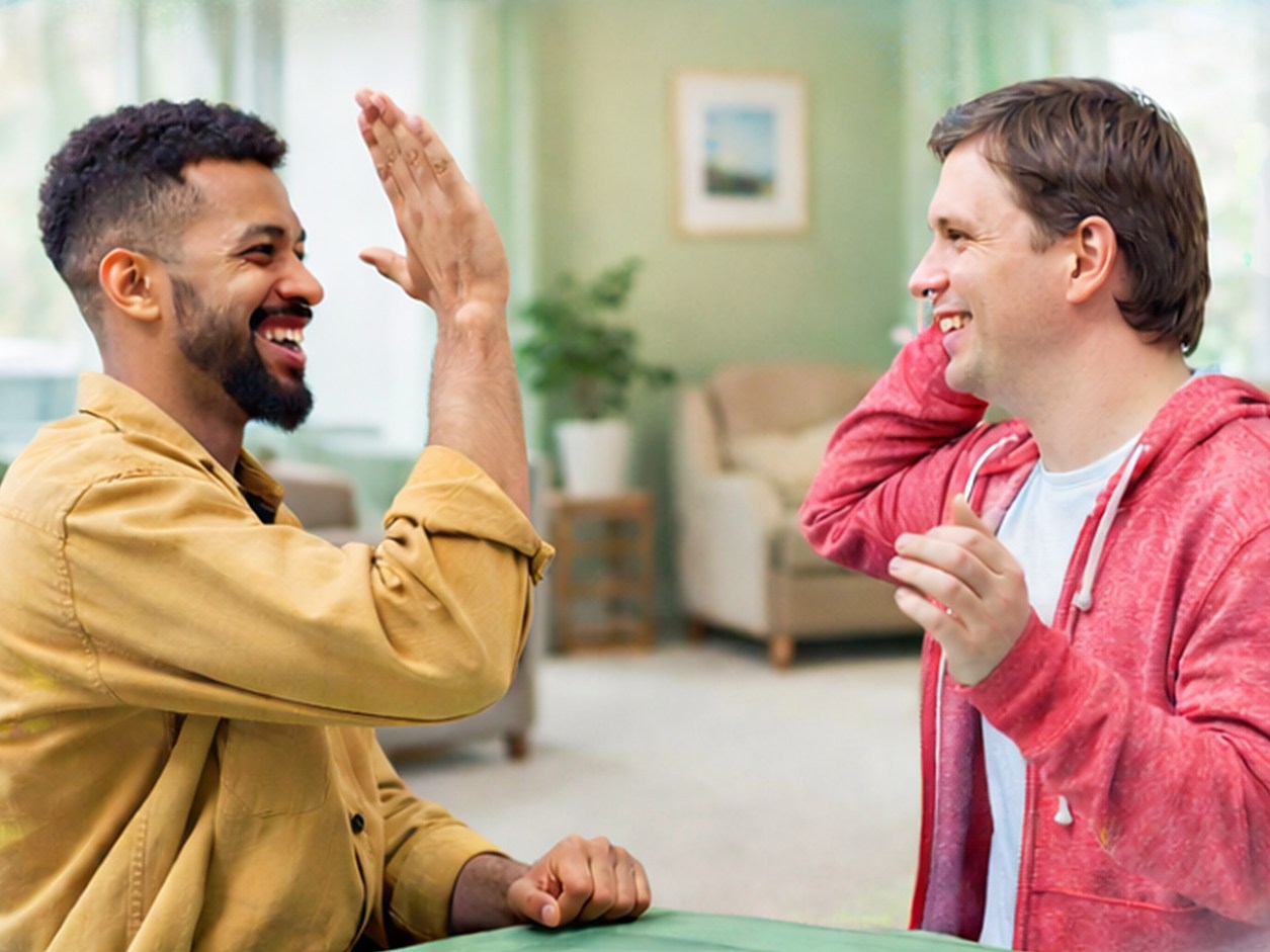 Two smiling men sharing a high five at a table in a bright lounge