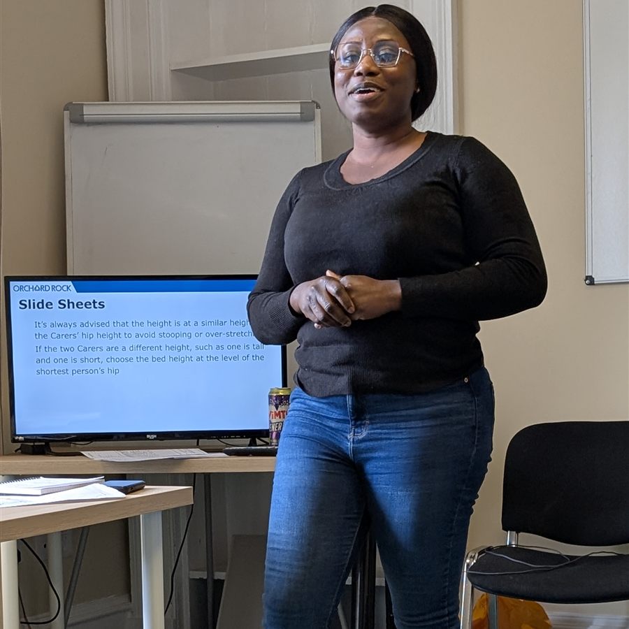 A trainee trainer teaching a session on slide sheets in front of a presentation screen